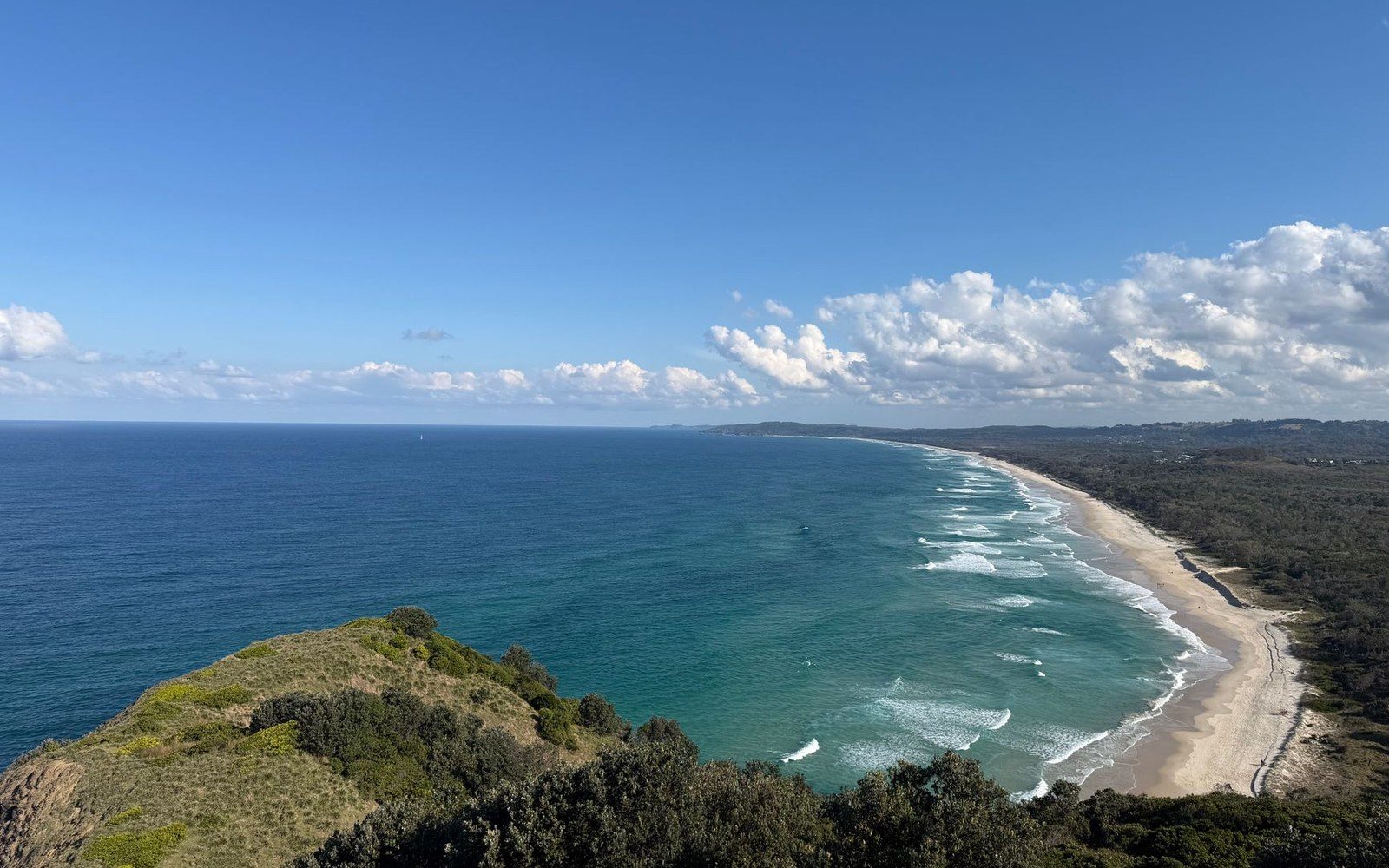 Aerial view of a curved sandy beach with turquoise waves meeting a grassy headland